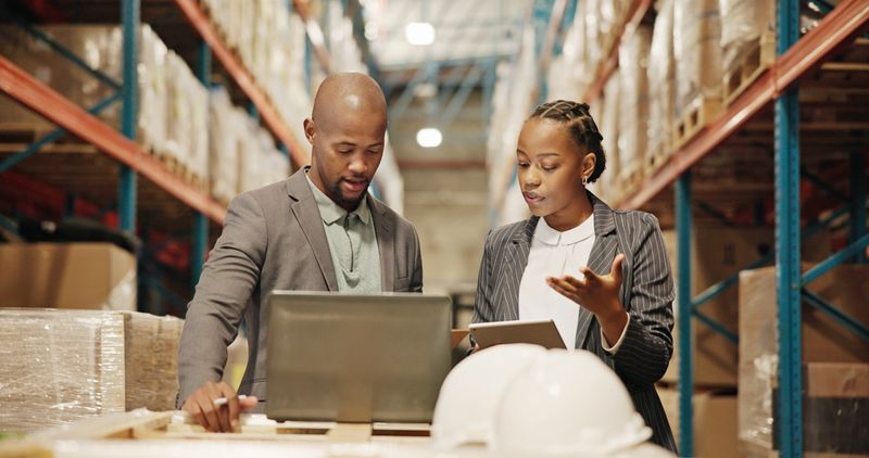 Collaboration, planning and people with laptop, factory or quality control for distribution with tech. Warehouse, teamwork and engineer with checklist for goods, logistics and discussion for shipping