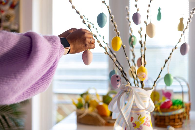 A medium detail shot of black hands placing an easter egg decoration onto a display. The display contains an array of colours in a house in the North East of England.Videos are available similar to this scenario.