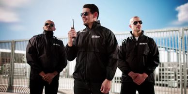 Three security guards wearing black jackets and sunglasses.
