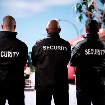 Three security guards stand facing away at an outdoor event.