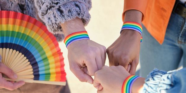 Three people wearing rainbow wristbands and forming a fist bump.
