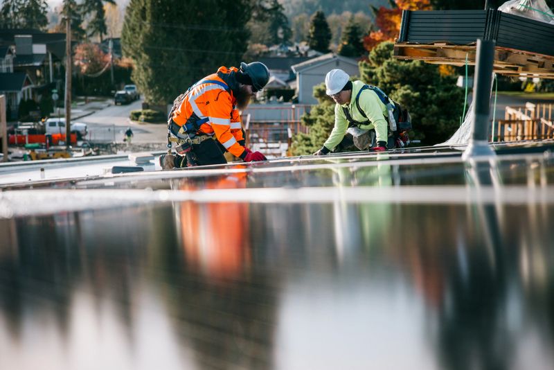A group of PV Installers (Solar Photovoltaic Installers) work on the roof of an apartment complex, equipping one of a number of buildings to be energy efficient and environmentally friendly.