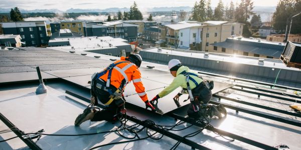 Two men working on a flat rooftop with metal rails and measuring tape.