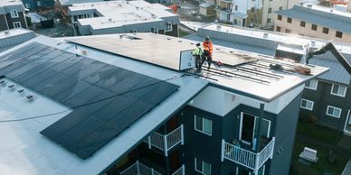 Workers installing solar panels on a flat rooftop of a residential building.