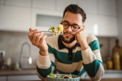 Man with glasses on sitting at a table eating a bowl of food 