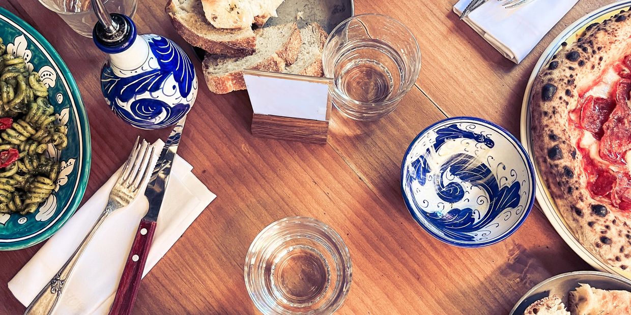 A rustic Italian meal with pasta, pizza, bread, and decorative blue bowls on a wooden table.