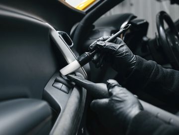 Person wearing gloves cleaning a car's interior button with a brush.