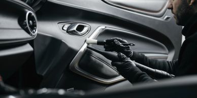 Man with gloves holding a gun inside a car.