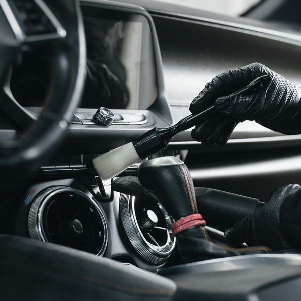 Person cleaning car interior vents with a brush while wearing black gloves.