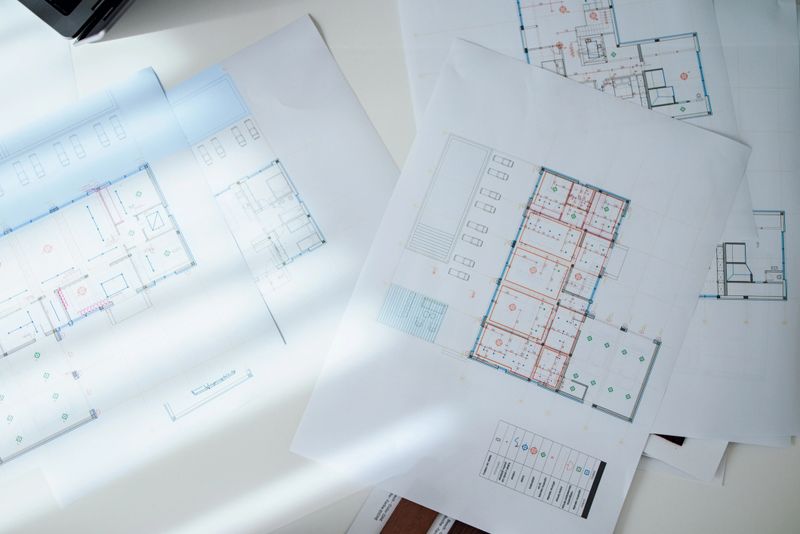 Detailed architectural blueprints and floor plans spread on a well-lit desk, showcasing creative designs and planning for construction or remodeling projects in a professional architecture or design studio setting.