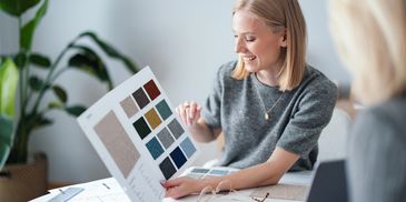 A woman happily showing fabric color samples to another person at a table.