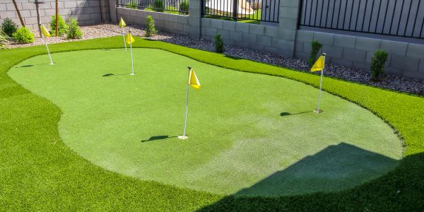 A backyard putting green with four yellow flags on synthetic grass.