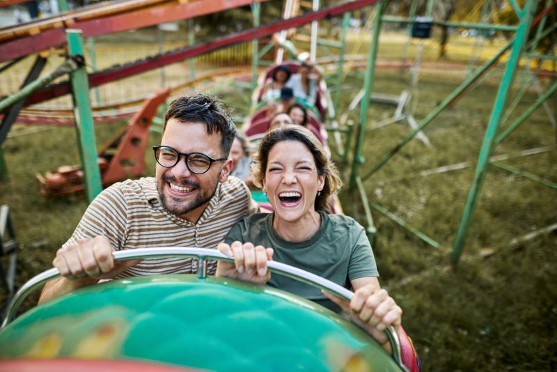 Happy couple having fun while riding on rollercoaster at amusement park.