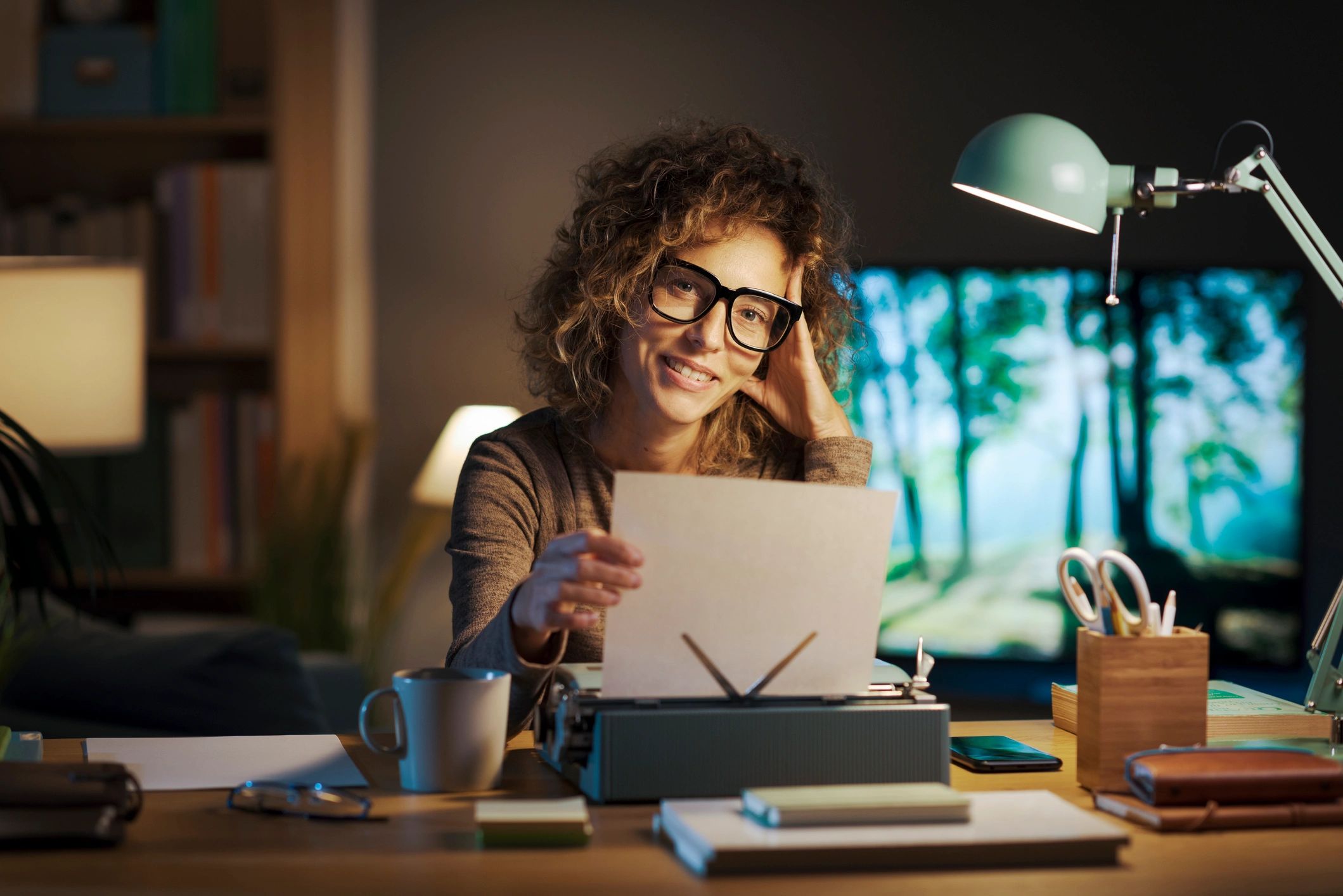 Author smiling at desk with typewriter, reviewing pages in a cozy, creative, and well-lit workspace.