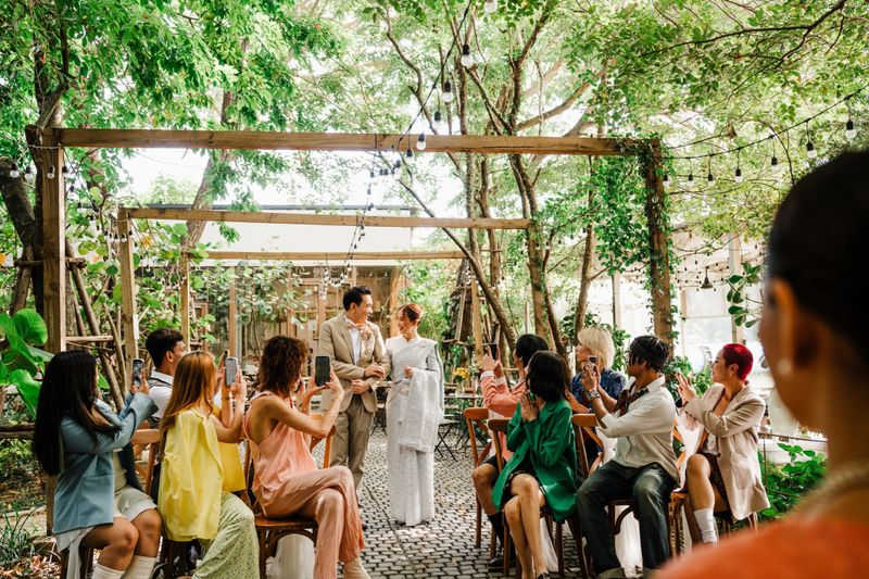 A joyful Thai wedding ceremony featuring the bride, father, and guests in a serene outdoor setting. Rustic charm, greenery, and cultural traditions create a vibrant celebration.