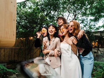 Five friends wearing colorful sunglasses joyfully posing outdoors.