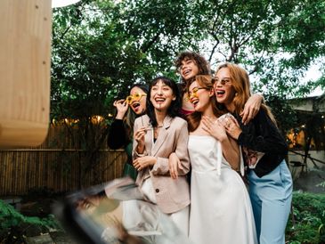 Five friends wearing colorful sunglasses joyfully posing outdoors.