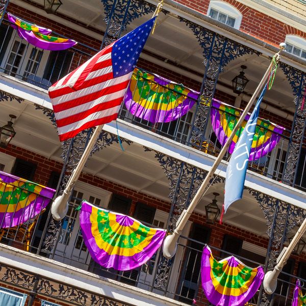 French Quarter balcony with U.S. flags and Mardi Gras decor in New Orleans event district.