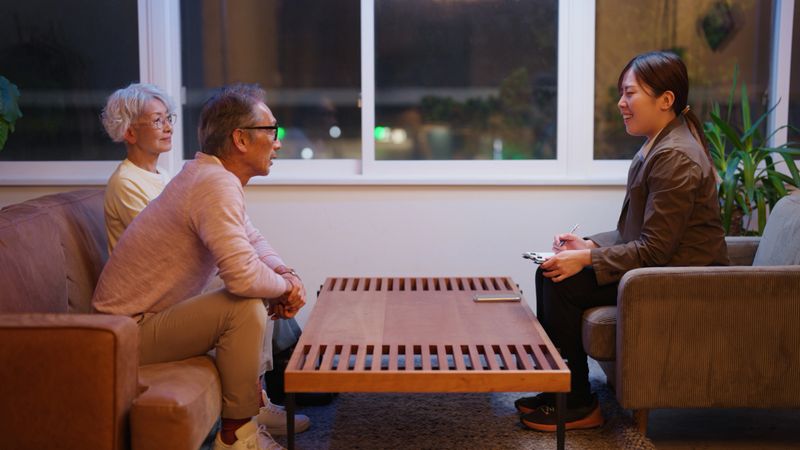 A senior couple attentively listens to a professional therapist during a counseling session in a warmly lit setting. The supportive environment highlights the importance of open communication, emotional well-being, and professional guidance in relationships and mental health.