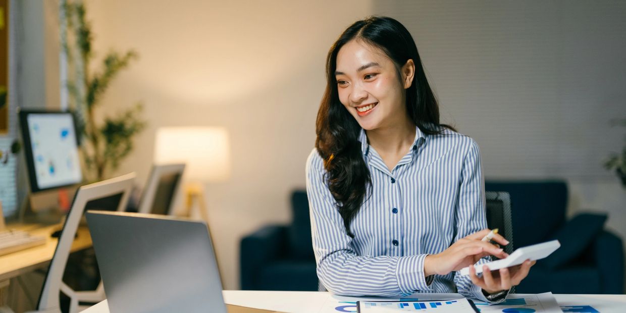 Woman working happily on laptop with calculator.