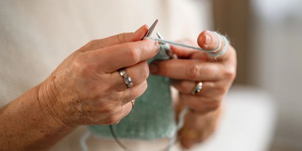 Hands knitting with blue yarn and needles.