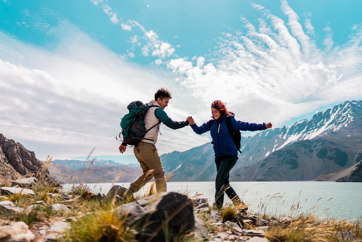 Two hikers enjoying a playful moment near a lake and mountains.