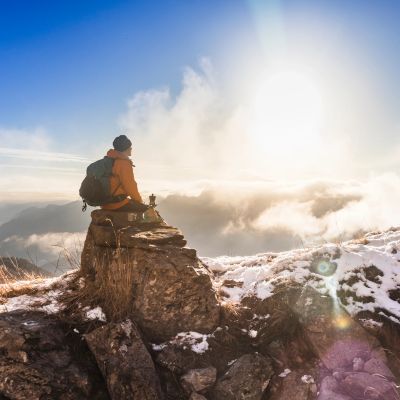 Person sitting on a rock, enjoying the sunrise above snowy mountains.