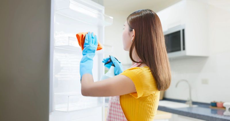 side view closeup asian woman clean up fridge interior - girl cleaning refrigerator with rag