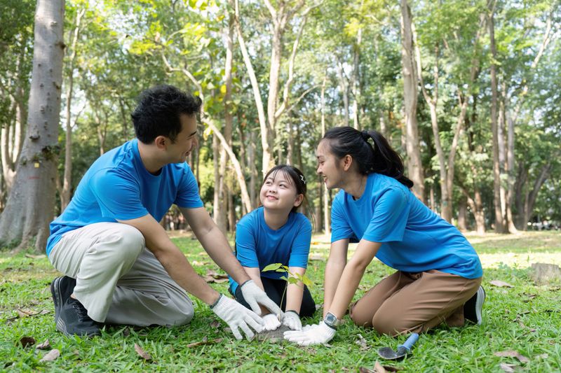 A cheerful family of volunteers engaged in planting a small tree in a lush park, highlighting their commitment to environmental conservation and teamwork.