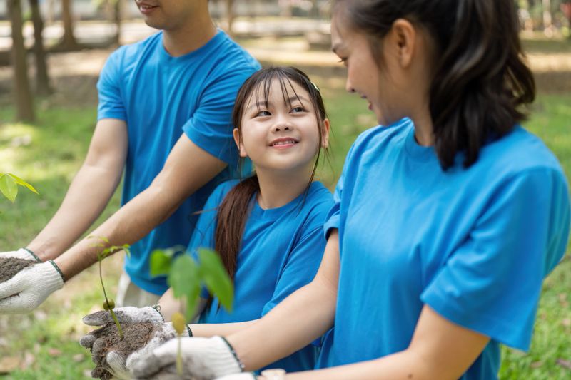 A joyful moment captured as family volunteers in blue shirts smile at each other while holding young trees, showcasing their commitment to environmental conservation.