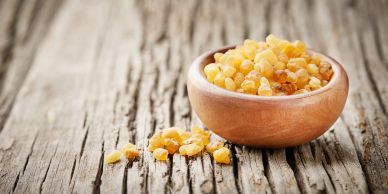 A wooden bowl filled with yellow resin pieces on a rustic wooden surface.