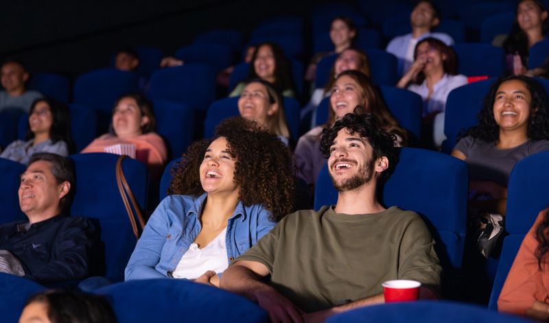Happy Latin American couple laughing while watching a funny movie at the theatre - lifestyles concepts