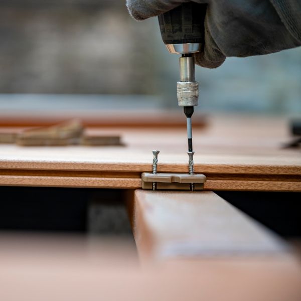 Screwing a deck board onto a wooden frame with a power drill.