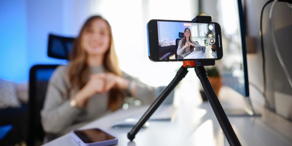 Woman recording a video on smartphone with tripod in a modern indoor setting.