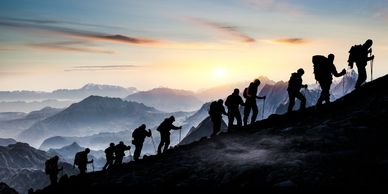 Silhouetted hikers ascending a mountain at sunrise.
