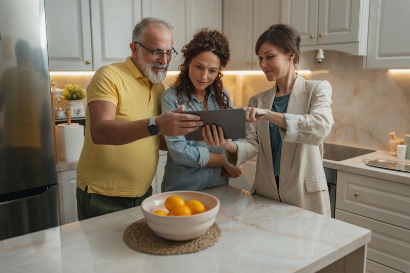 A team of three adults, engaged in a collaborative discussion over a tablet, emphasize shared ideas in a stylish kitchen ambiance, creating a productive environment.