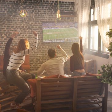 Three friends cheer while watching a football game on TV in a cozy living room.