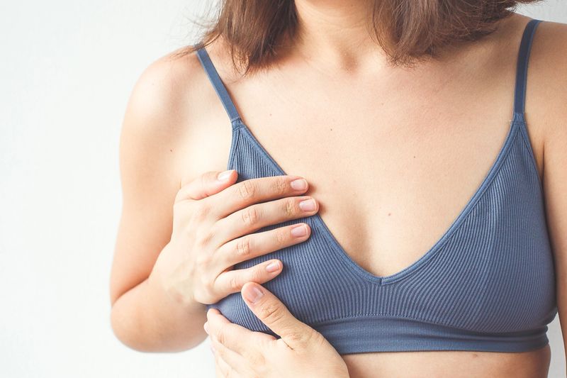 Woman holding her breast with both hands, illustrating discomfort or pain, possibly related to breast health issues such as mastitis, lumps, or hormonal changes, isolated against a white background