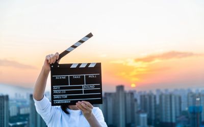 Person holding a film clapperboard with a city skyline at sunset.