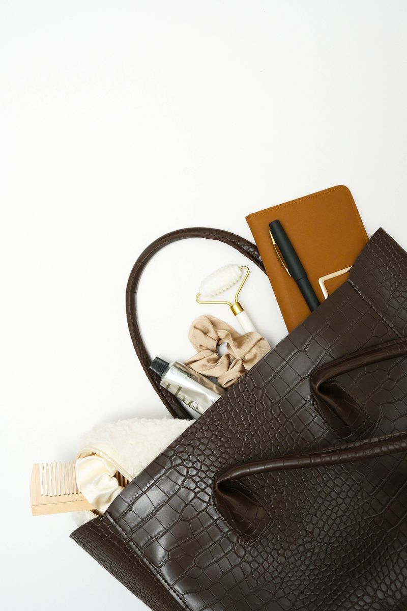 Chic and Stylish Brown Handbag with all Essential Items: makeup bag, hairbrush, notebook, pen laid Out Inside on white background. High quality photo