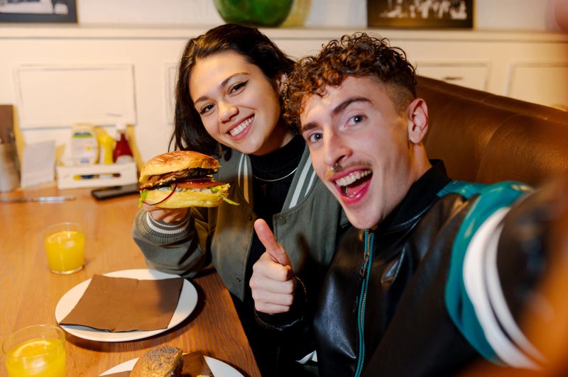 Young couple taking a selfie while enjoying burgers and orange juice in a restaurant