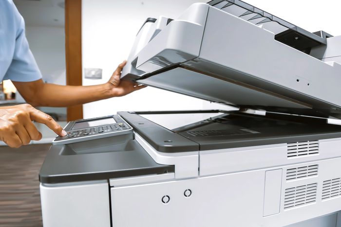 A person using a photocopier machine with the lid open.