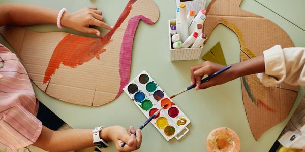 Two people painting cardboard cutouts with watercolors and markers.