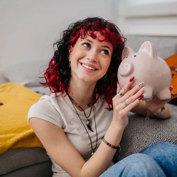 Smiling woman holding a piggy bank, sitting on a couch with a guitar in the background.