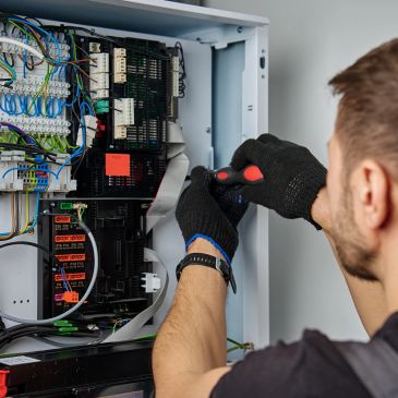 Technician fixing electrical control panel with screwdriver and gloves.