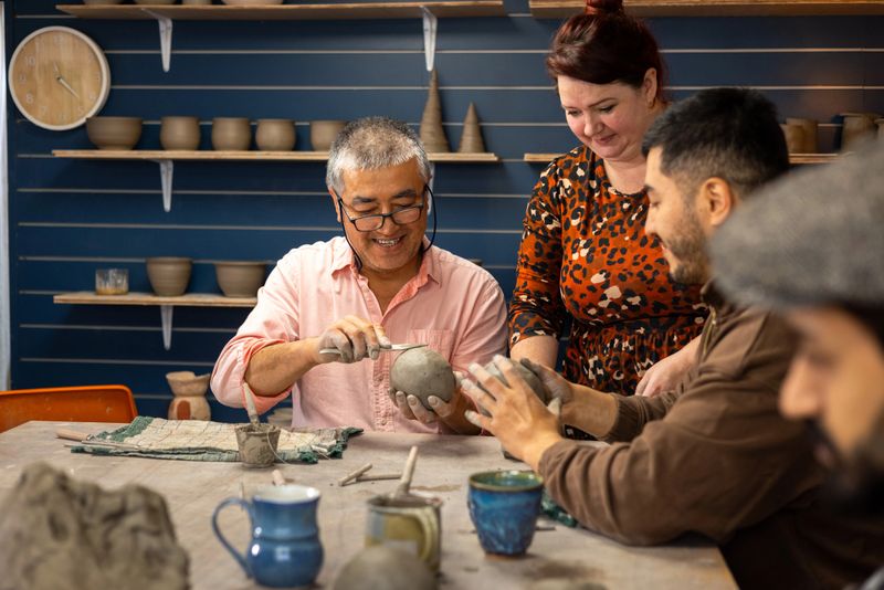 A medium shot of a father and son enjoying a pottery class together, guided by a friendly instructor in a cosy studio filled with handmade ceramics. They smile and engage in the creative process, shaping clay with enthusiasm. 

Videos are available similar to this scenario.