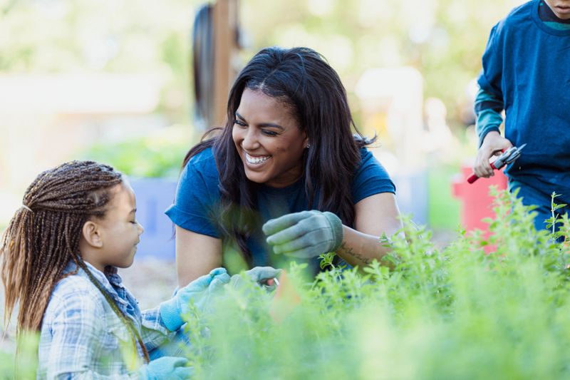 Smiling woman and child volunteer working in community garden.  Active lifestyle, teamwork, and emotional support.