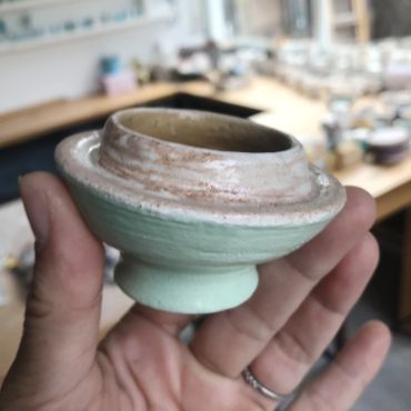 Hand holding a small ceramic pottery piece.