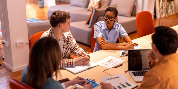 A diverse group discussing business charts around a table in a modern office.
