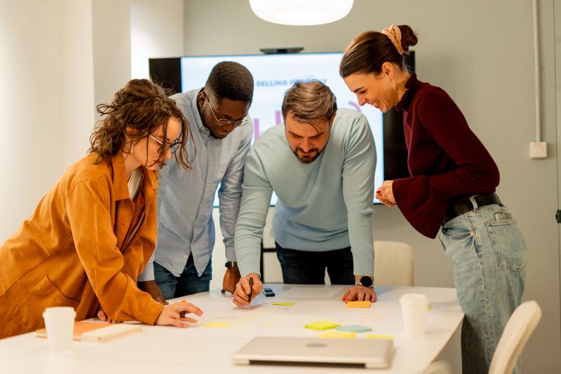 Diverse group of young professionals collaborates on a marketing strategy, using sticky notes and a whiteboard to visualize their ideas in a modern office setting